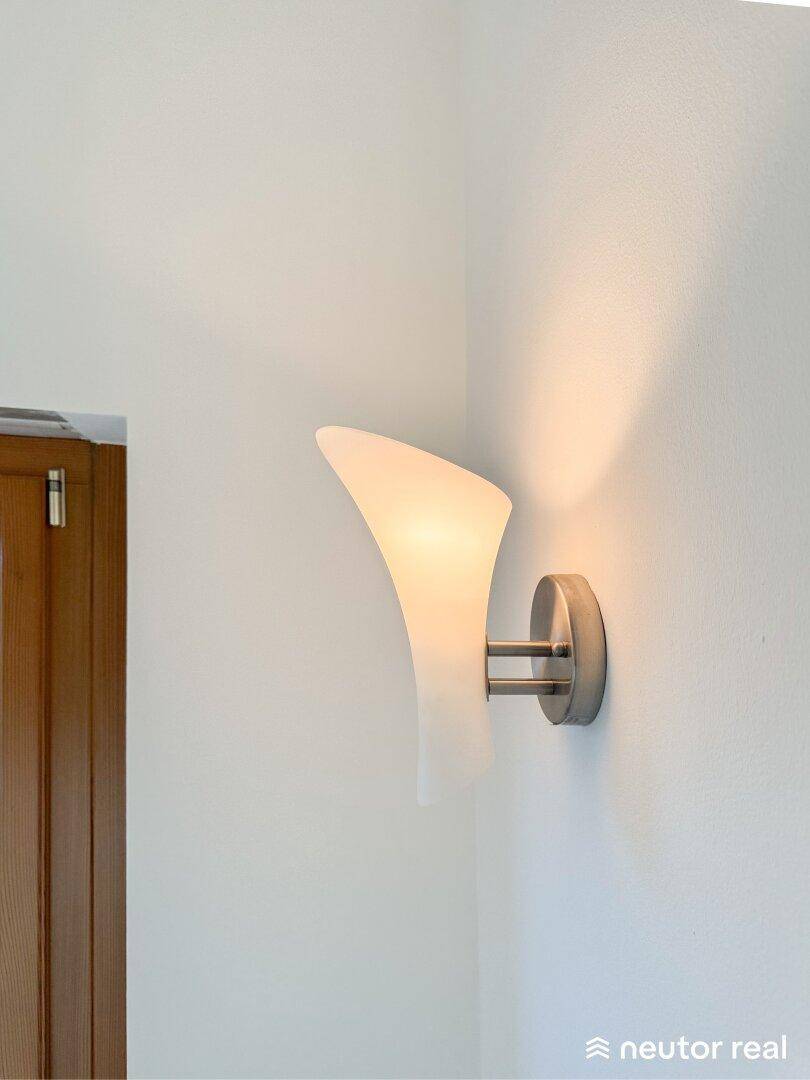 Detailaufnahme einer modernen Wandleuchte mit diffusem Licht an einer weißen Wand.