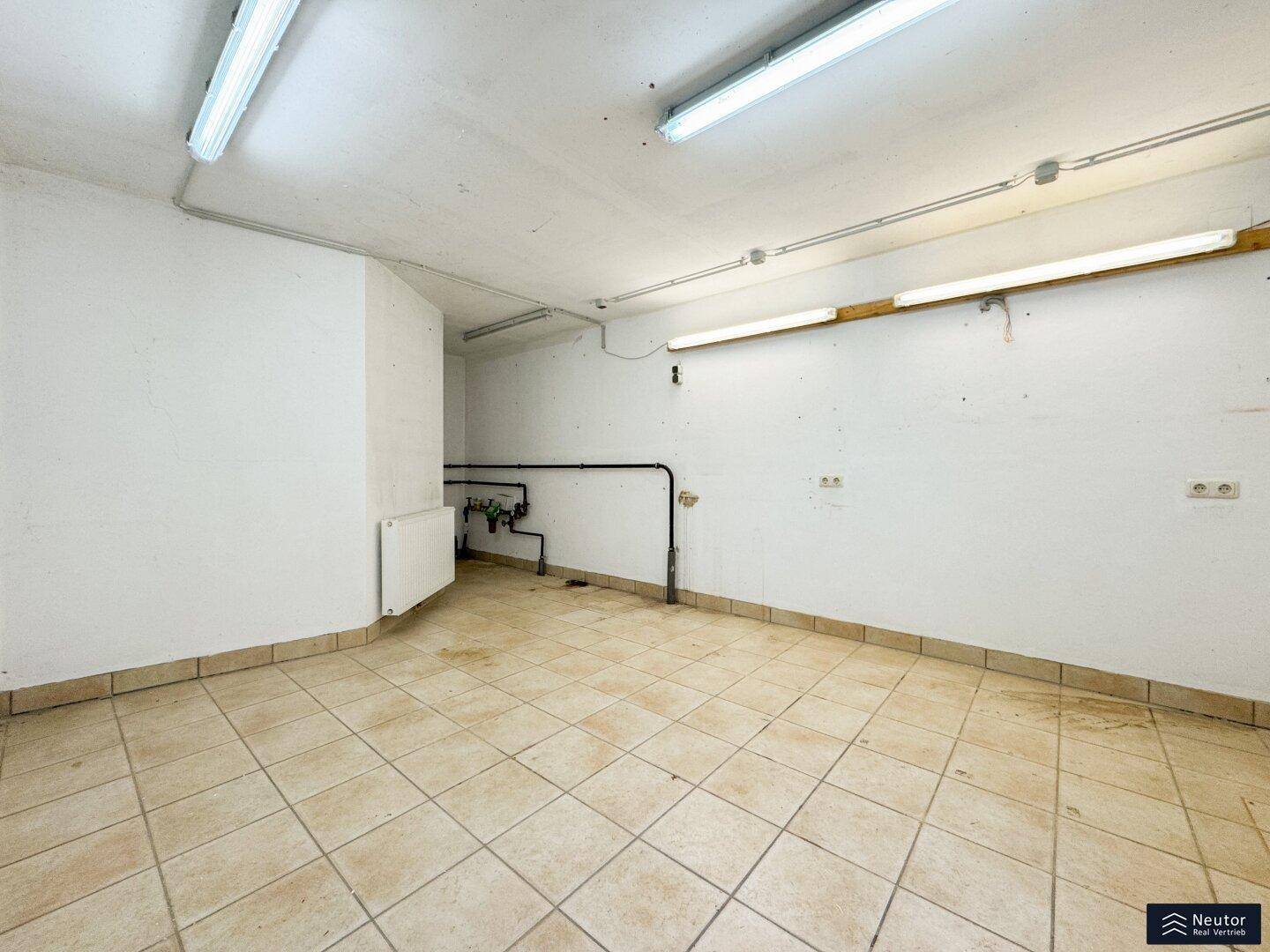 Geräumiger Kellerraum mit Fliesenboden, weißen Wänden und sichtbaren Installationen.