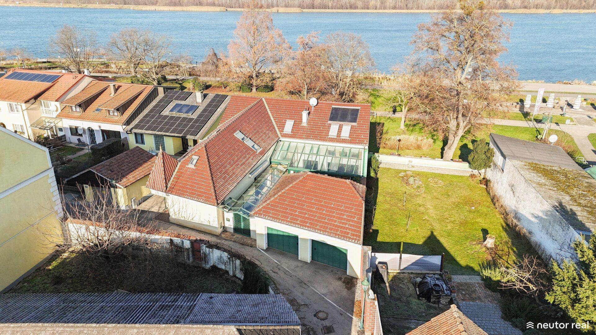 Luftaufnahme eines Hauses mit Garten, Garagen und Blick auf den See.
