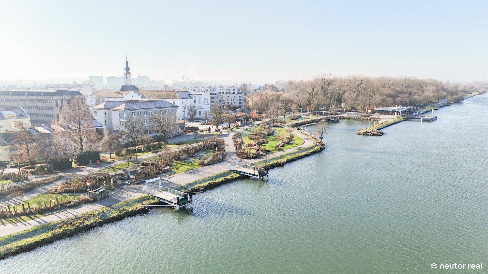 Weitläufige Luftaufnahme einer Stadtlandschaft mit einem Fluss, Grünflächen und Gebäuden unter klarem Himmel.