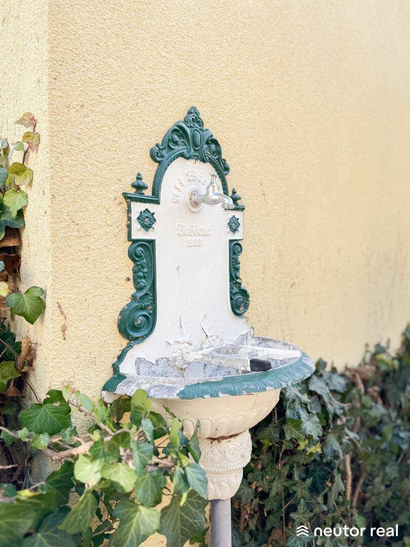 Dekorative Wandfontäne im Vintage-Stil an einer gelben Hauswand.