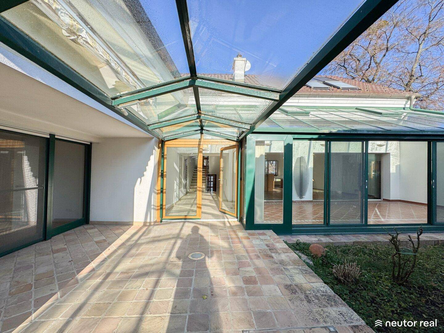 Überdachter Übergang mit Glasdach und großen Schiebetüren, der zu einem Wintergarten führt.