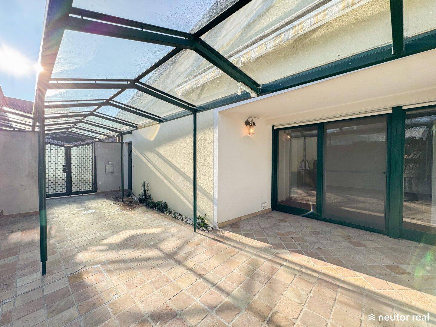 Überdachte Terrasse mit Fliesenboden und Zugang zum Haus.