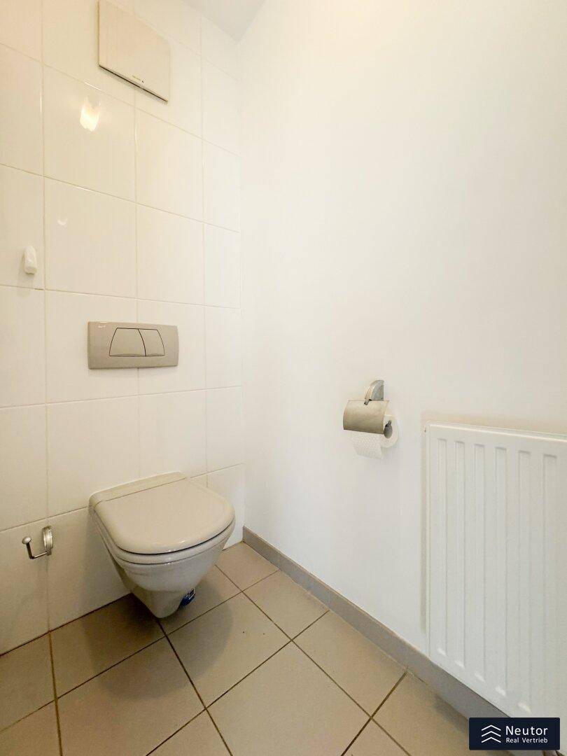Modernes WC mit Wand-WC, Spülkasten und weißen Fliesen an Wänden und Boden.