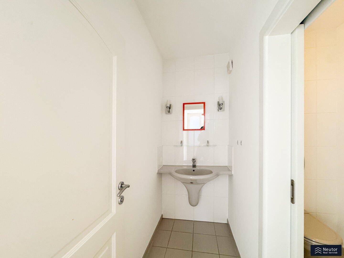 Helles Gäste-WC mit Waschbecken, Spiegel und weißen Wandfliesen.