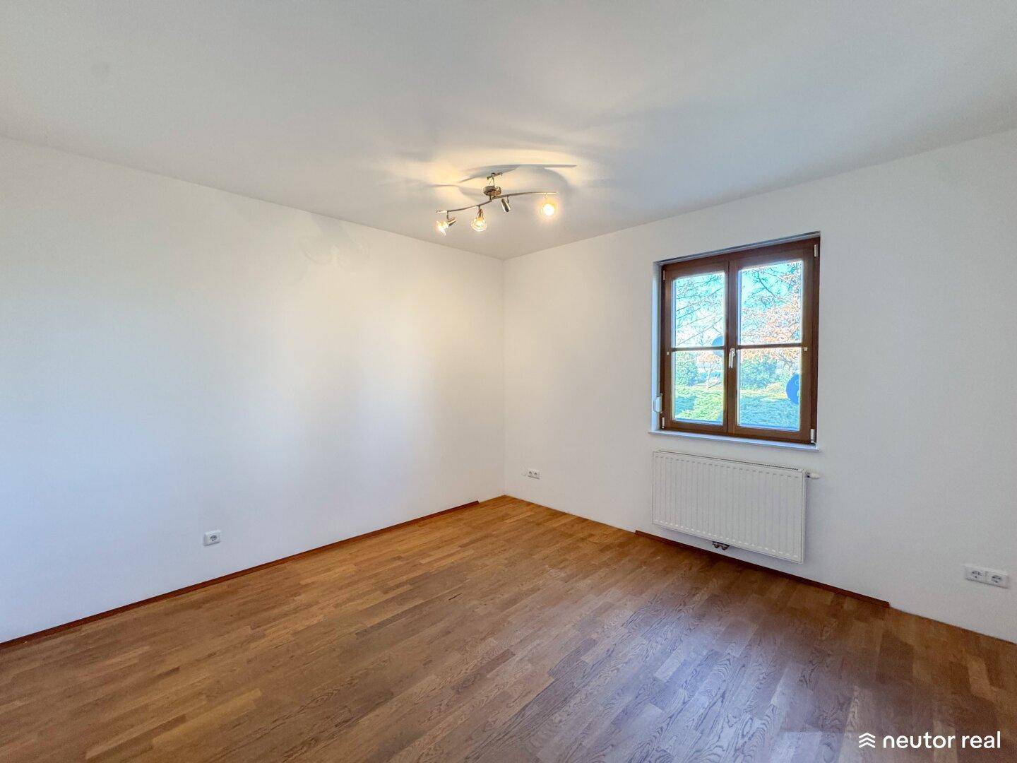 Helles Zimmer mit Parkettboden und einem Fenster, das viel Tageslicht hereinlässt.
