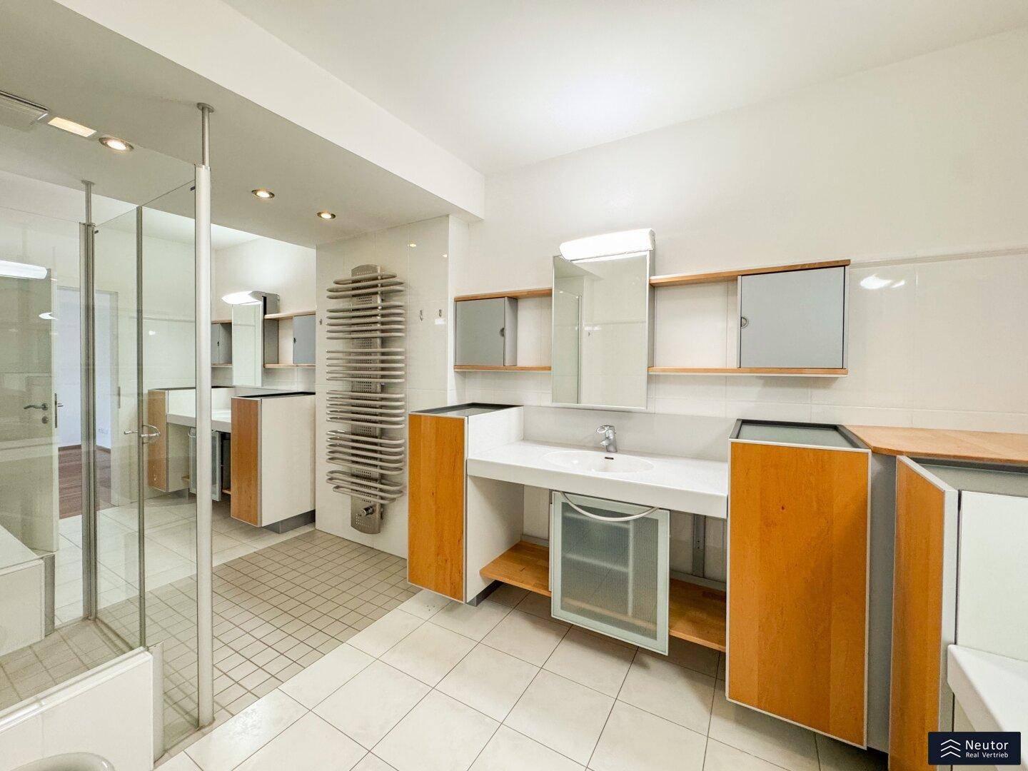 Geräumiges Badezimmer mit Doppelwaschbecken, Dusche und beheiztem Handtuchhalter.