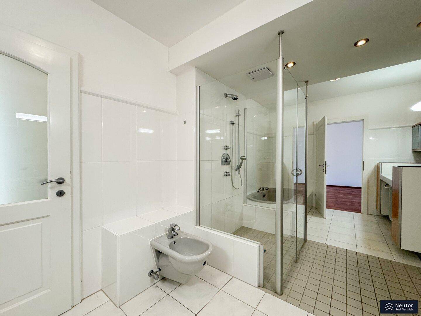 Helles Badezimmer mit Duschkabine, Bidet und weißen Fliesen an Wänden und Boden.