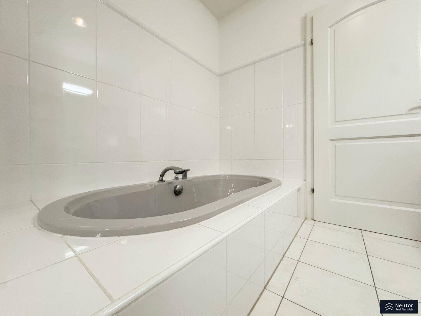 Badezimmer mit eingebauter Badewanne und weißen Fliesen, die eine saubere Optik schaffen.