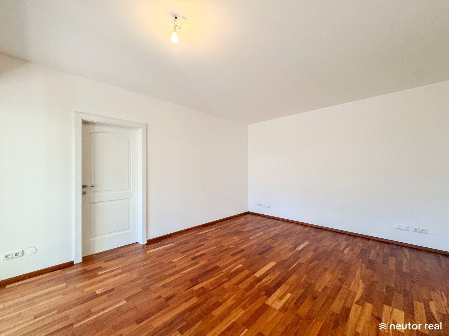 Geräumiges Schlafzimmer mit warmem Parkettboden und weiß gestrichenen Wänden, bereit zur Einrichtung.