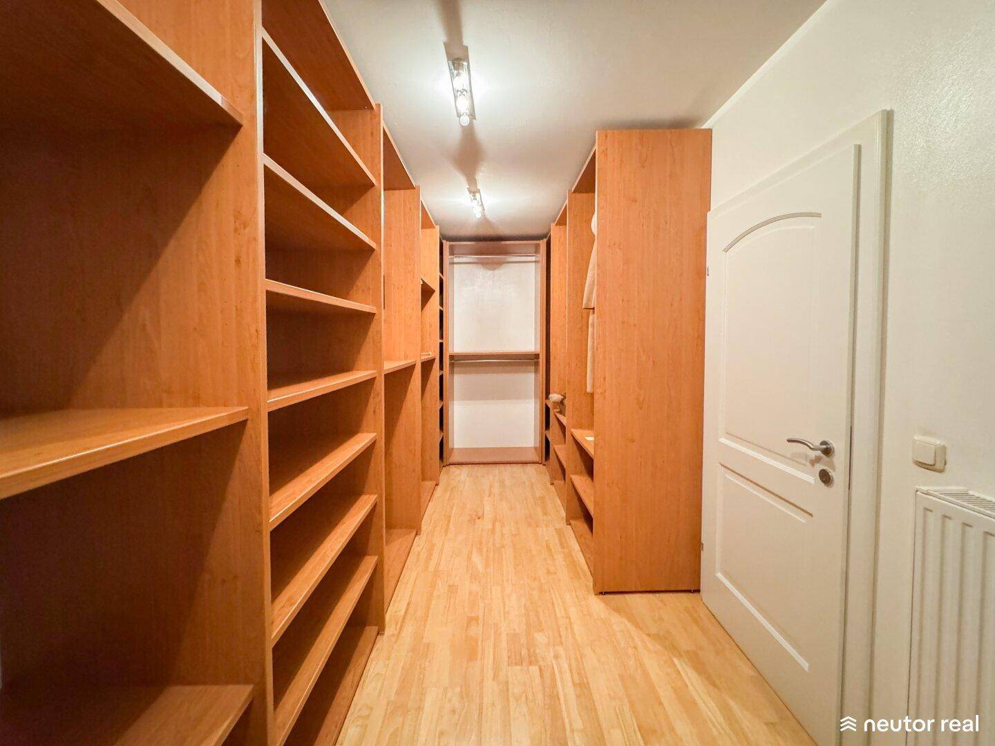 Geräumiger begehbarer Kleiderschrank mit zahlreichen Holzregalen und viel Platz für Kleidung.