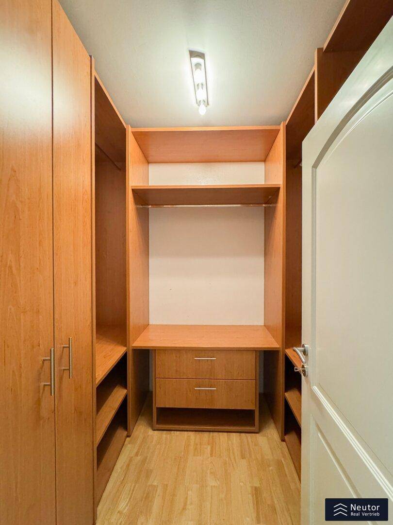 Praktischer begehbarer Kleiderschrank mit Holzregalen und Schubladen für viel Stauraum.