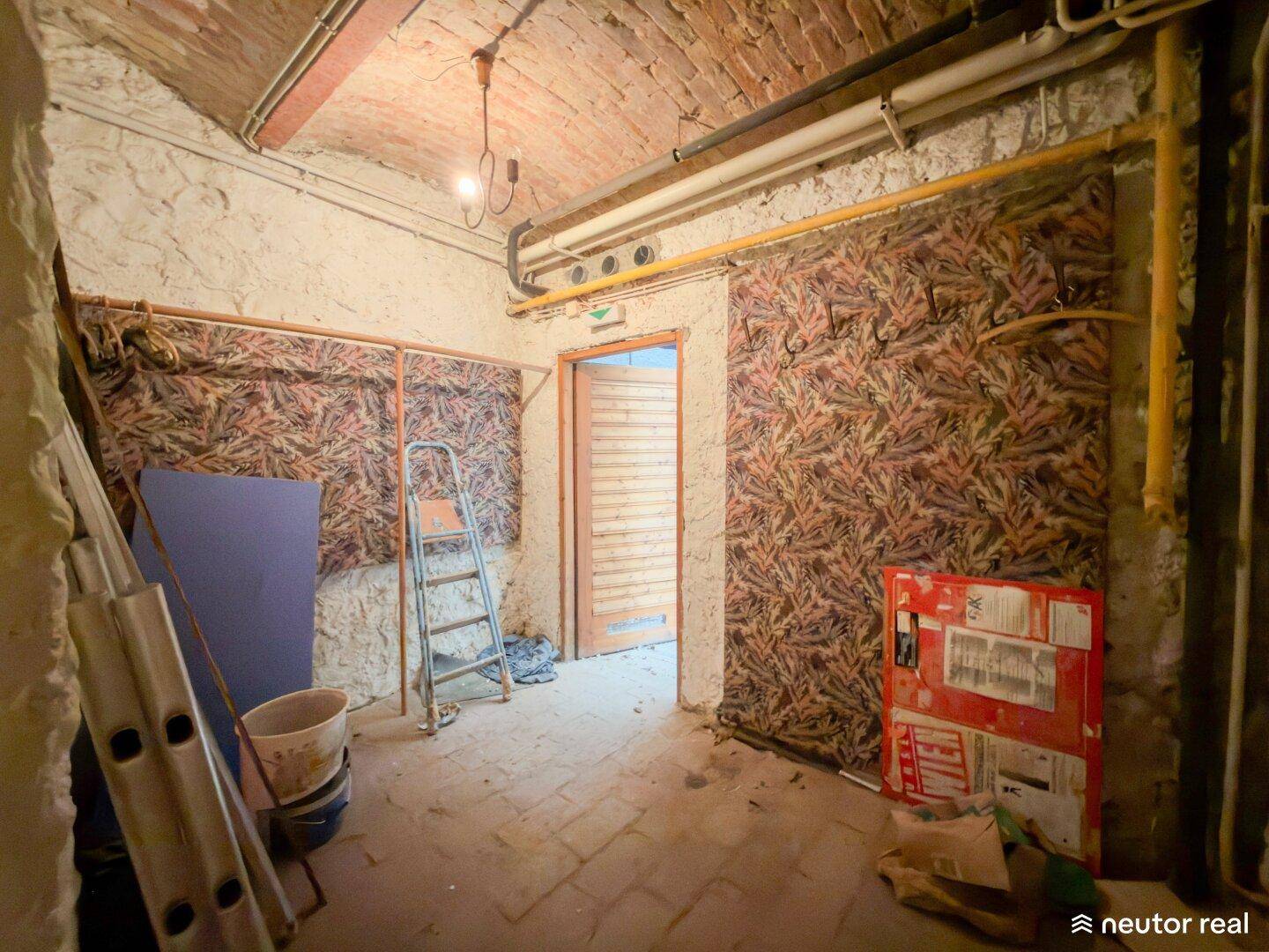 Lagerraum im Keller mit rustikalen Wänden, freiliegenden Rohren und einer Holztür.