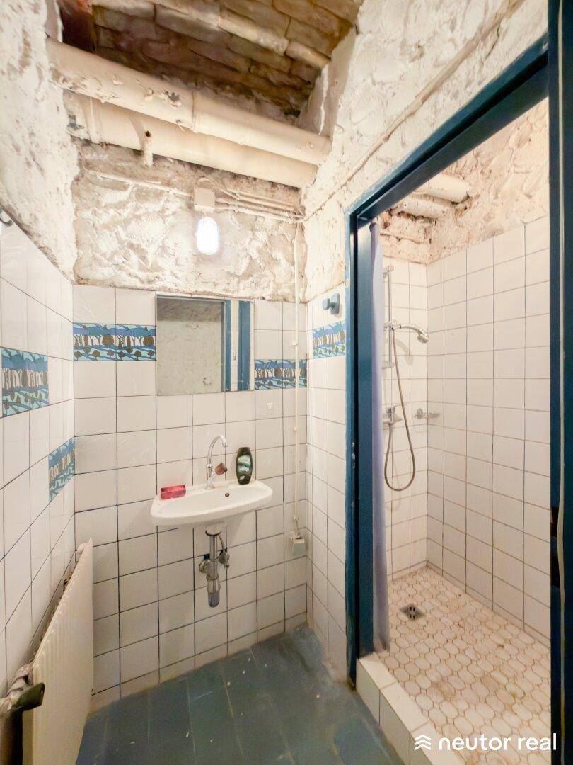 Einfaches Badezimmer mit Waschbecken, Spiegel und einer Duschkabine mit Fliesenboden.