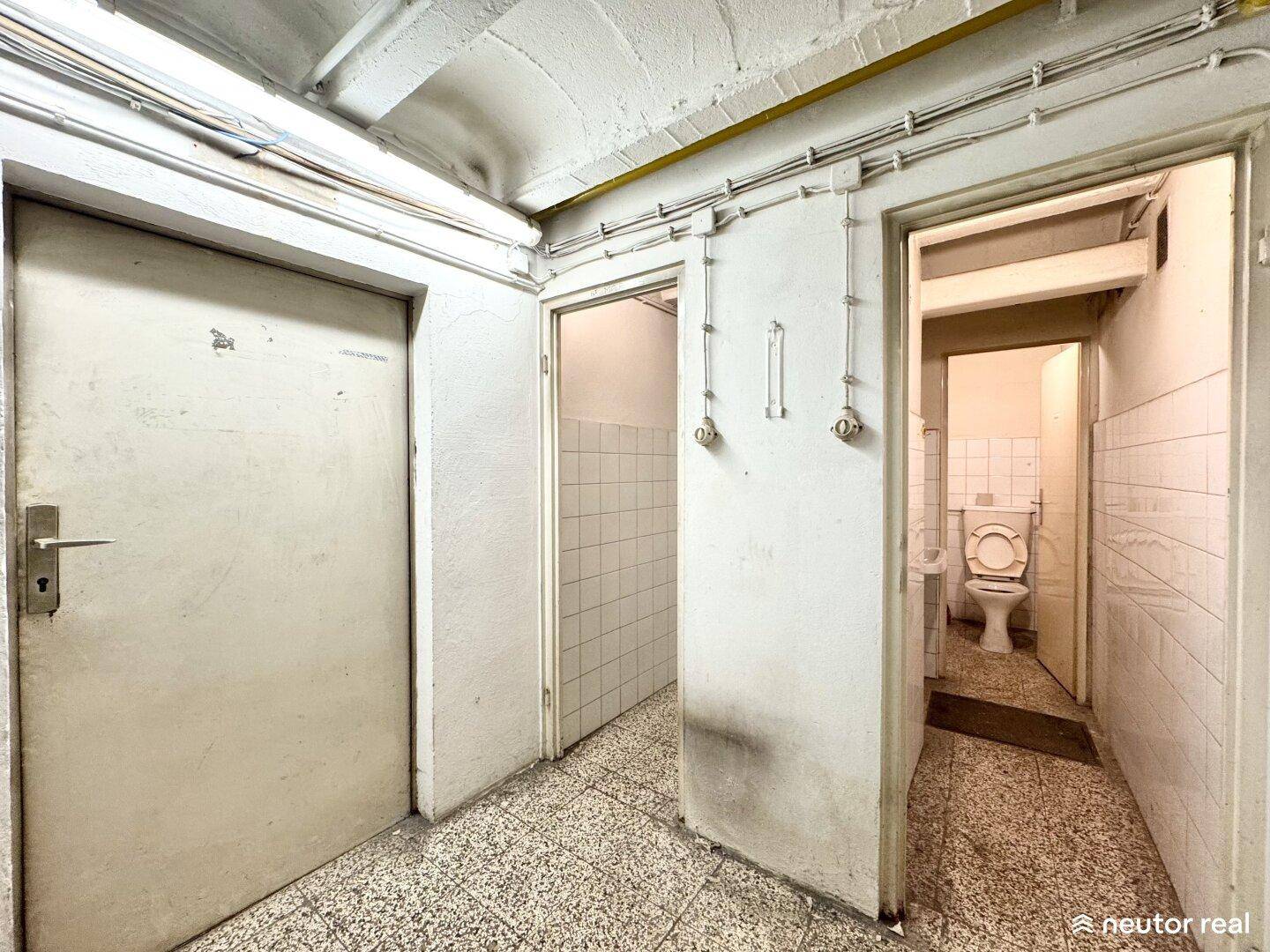 Kellerflur mit mehreren Türen, eine davon führt zu einer Toilette, auf einem Terrazzo-ähnlichen Boden.