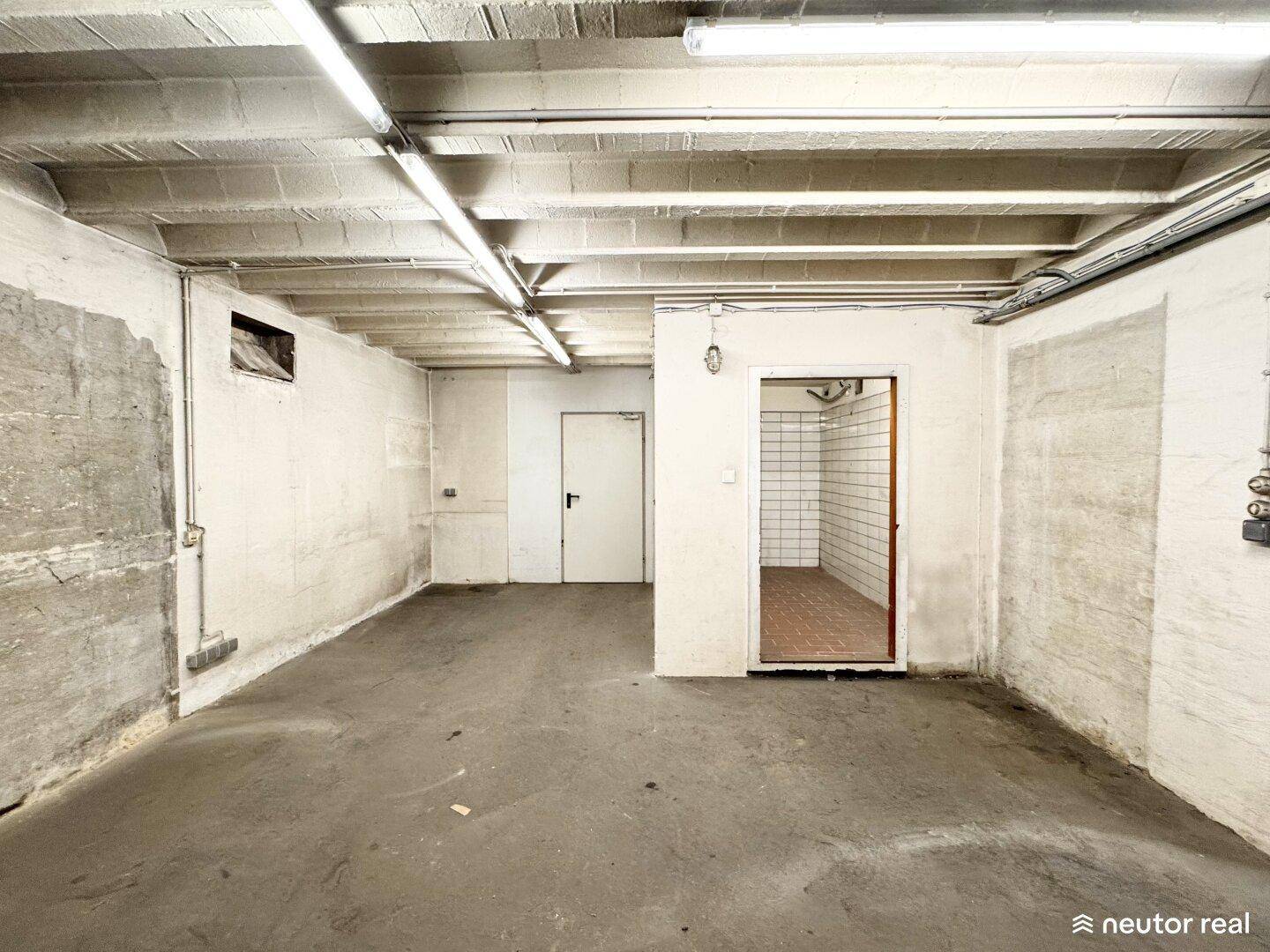 Weiterer Blick in den Kellerbereich mit Betonboden und Zugang zu einem gefliesten Nebenraum.