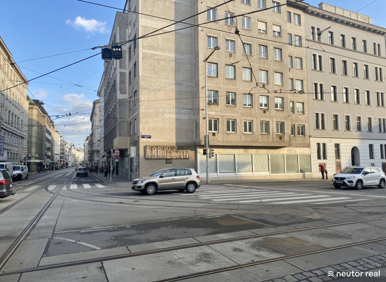 Stadtansicht einer belebten Kreuzung mit Gebäuden und Fahrzeugen unter blauem Himmel.