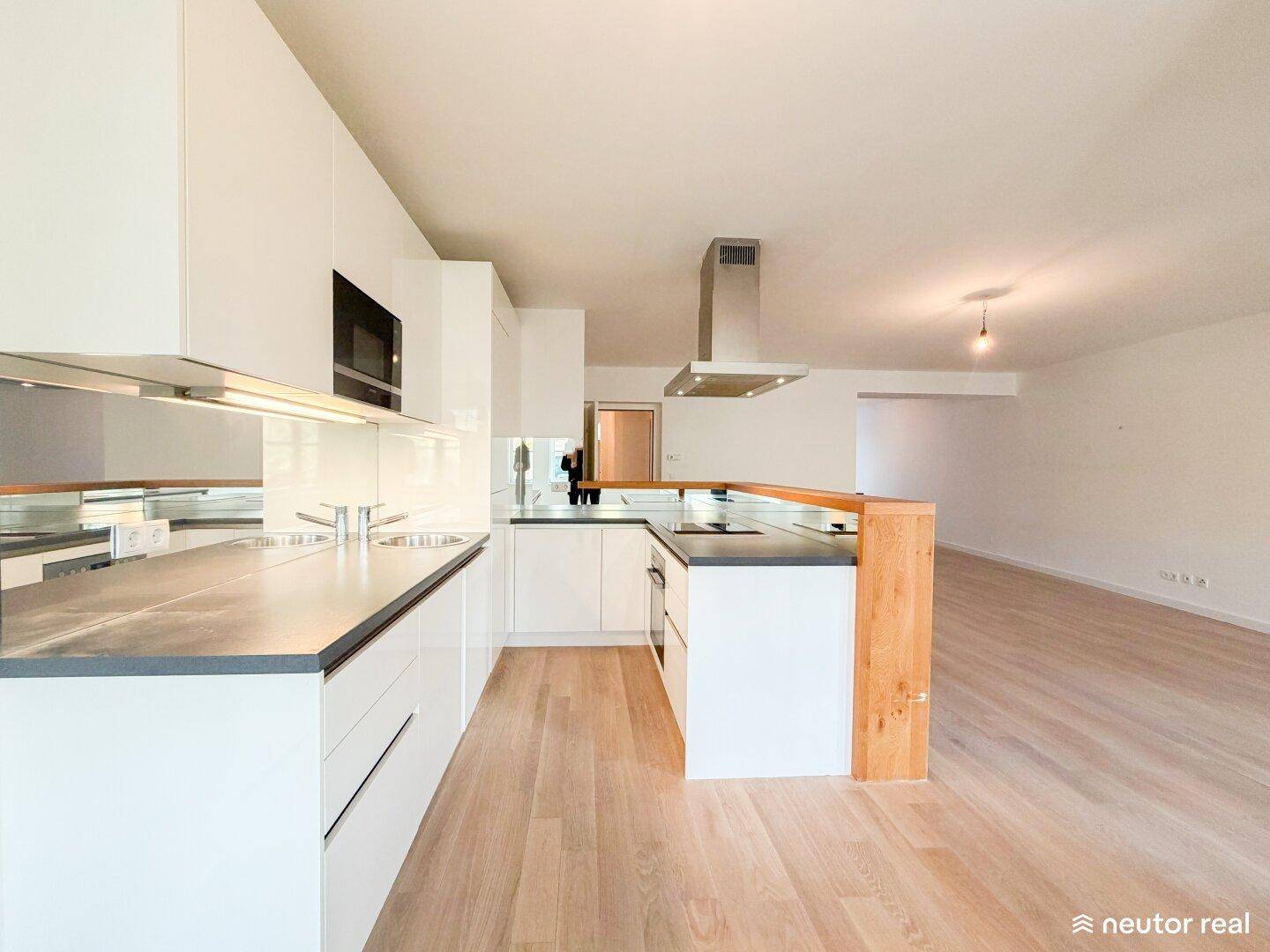 Moderne Einbauküche mit weißen Hochglanzfronten, dunklen Arbeitsplatten und Dunstabzugshaube.