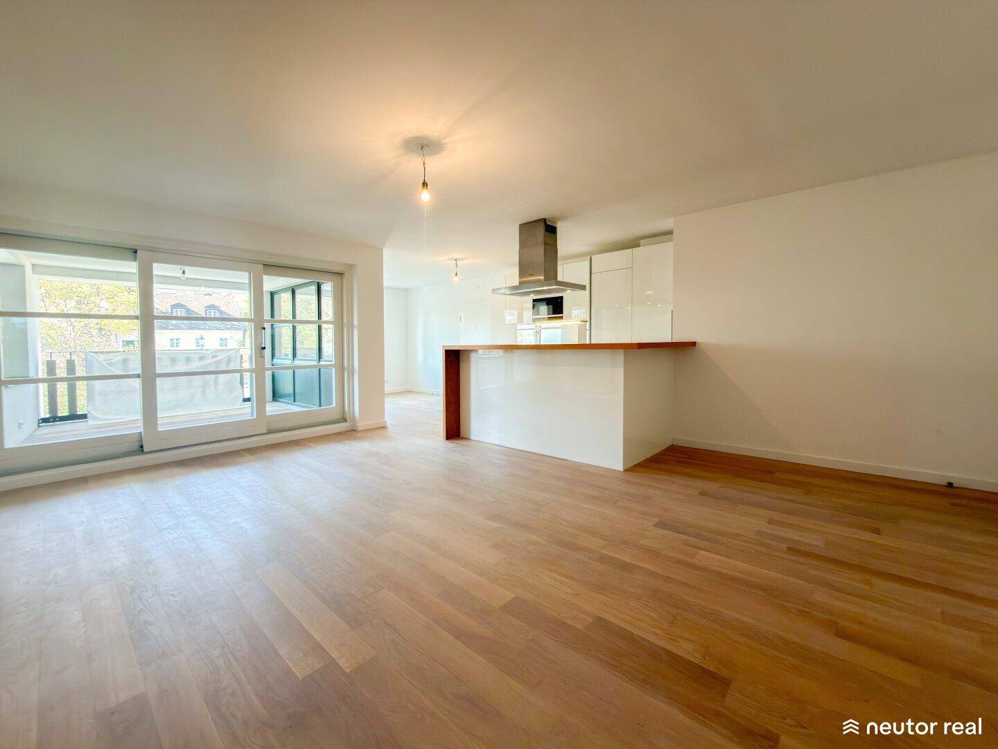 Offener Wohnbereich mit Holzboden, Küchenzeile und Zugang zu einem Balkon.