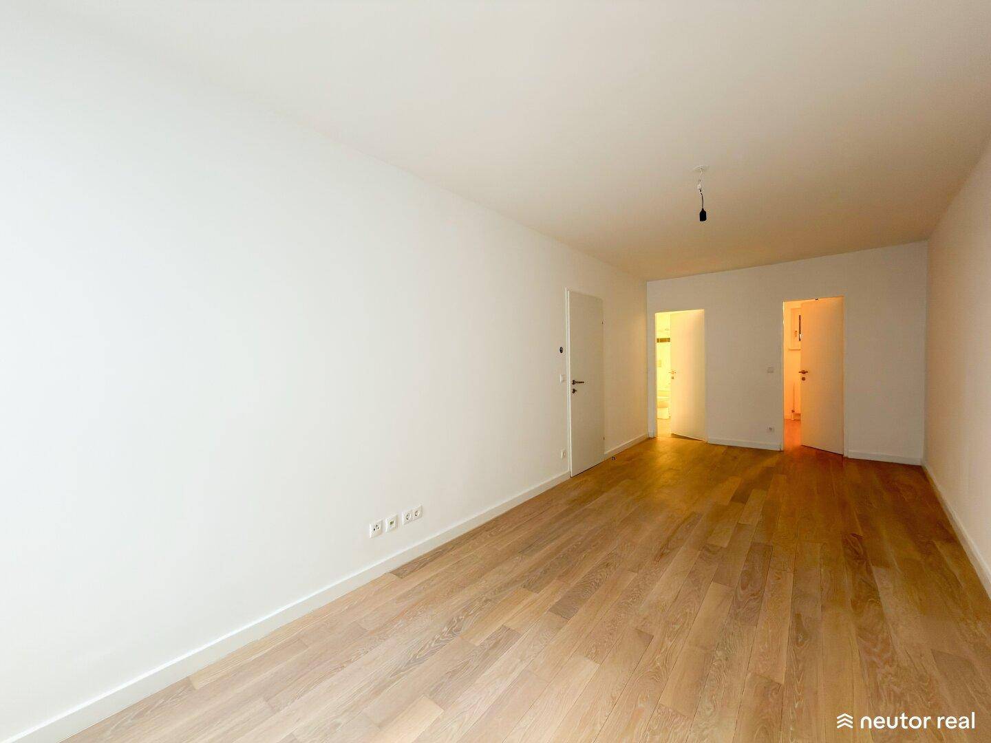 Geräumiger, heller Raum mit Holzboden und Zugang zu weiteren Zimmern.