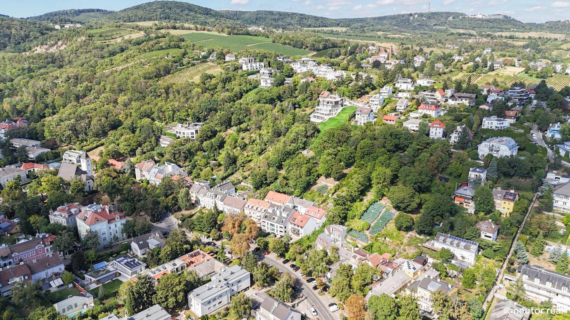 Luftaufnahme einer Wohngegend mit vielen Bäumen und Häusern in hügeliger Landschaft.