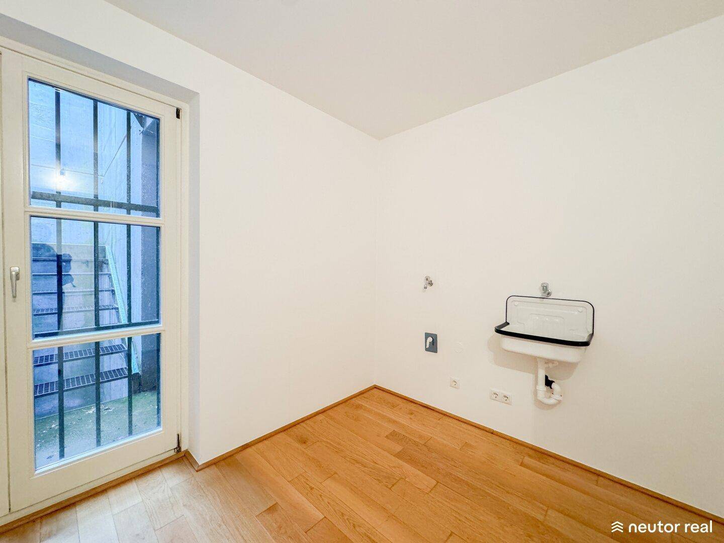 Hauswirtschaftsraum mit Waschbecken, Holzboden und Zugang zum Außenbereich.