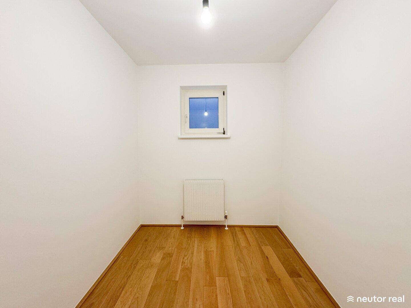 Kleiner, heller Raum mit Holzboden und Fenster, ideal als Büro oder Kinderzimmer.