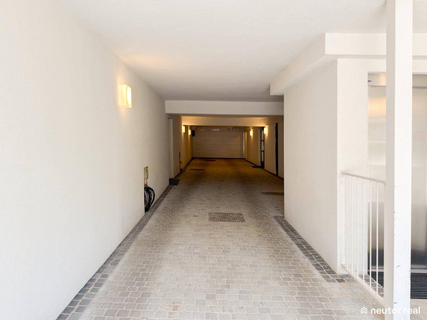 Einfahrt zur Tiefgarage mit gepflastertem Weg und Beleuchtung an den Wänden.