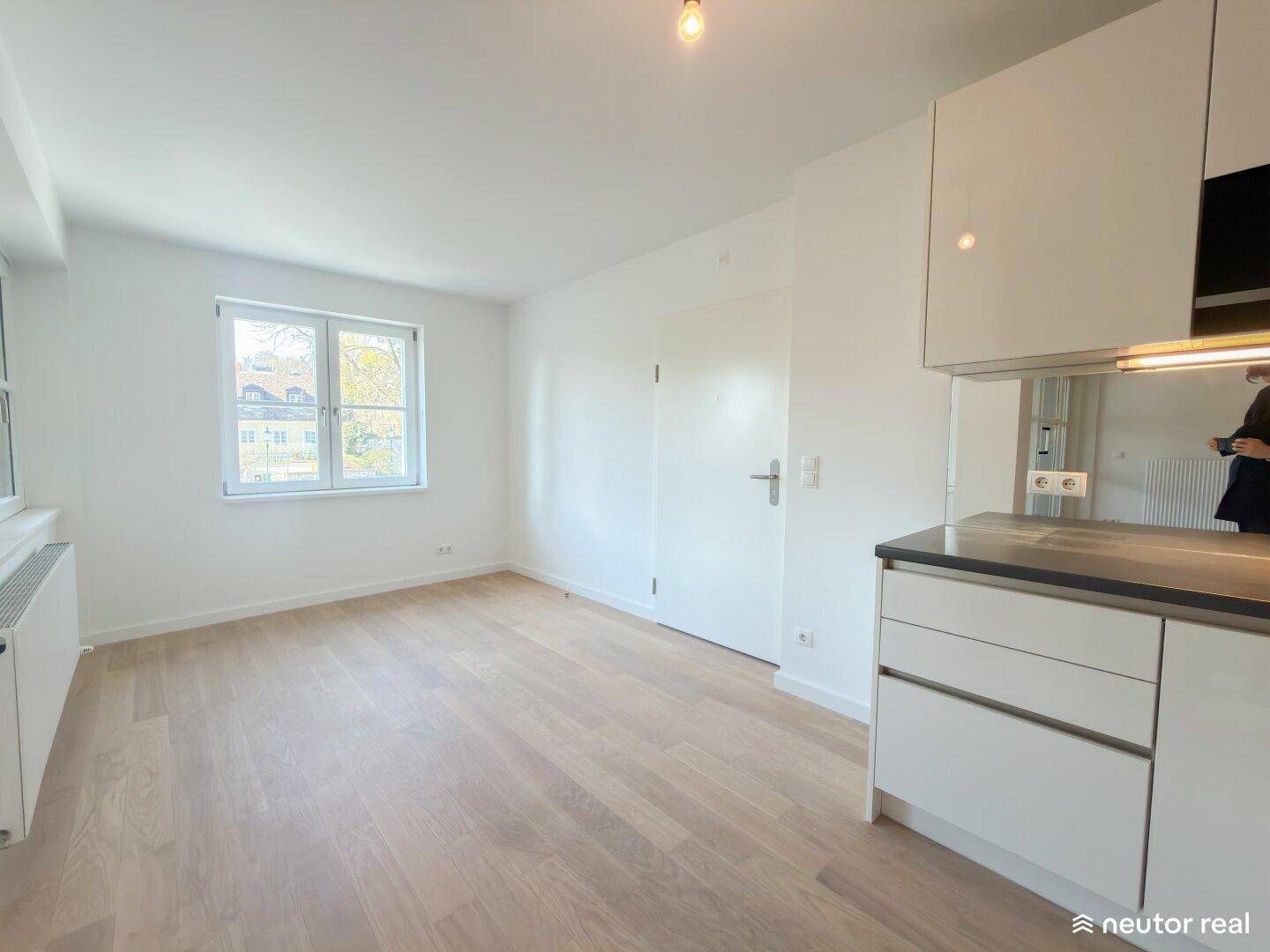 Offener Küchenbereich mit weißen Schränken, Holzboden und Fensterblick.