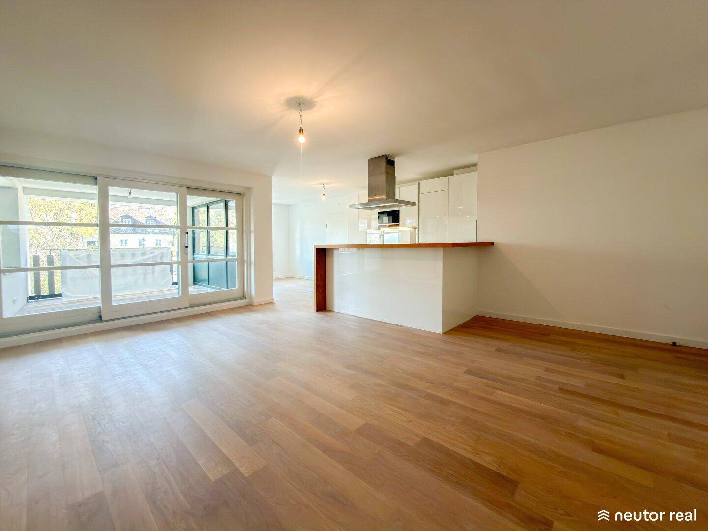 Geräumiger Wohnbereich mit offener Küche, Holzboden und Zugang zum Balkon.