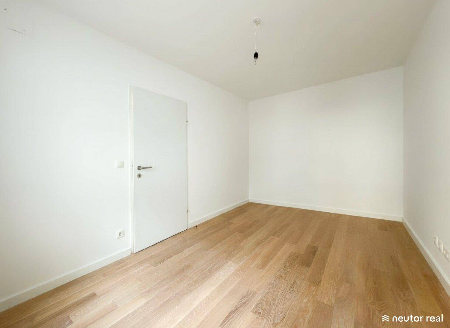 Leeres Schlafzimmer mit hellem Holzboden und weißer Tür, bereit zur Einrichtung.