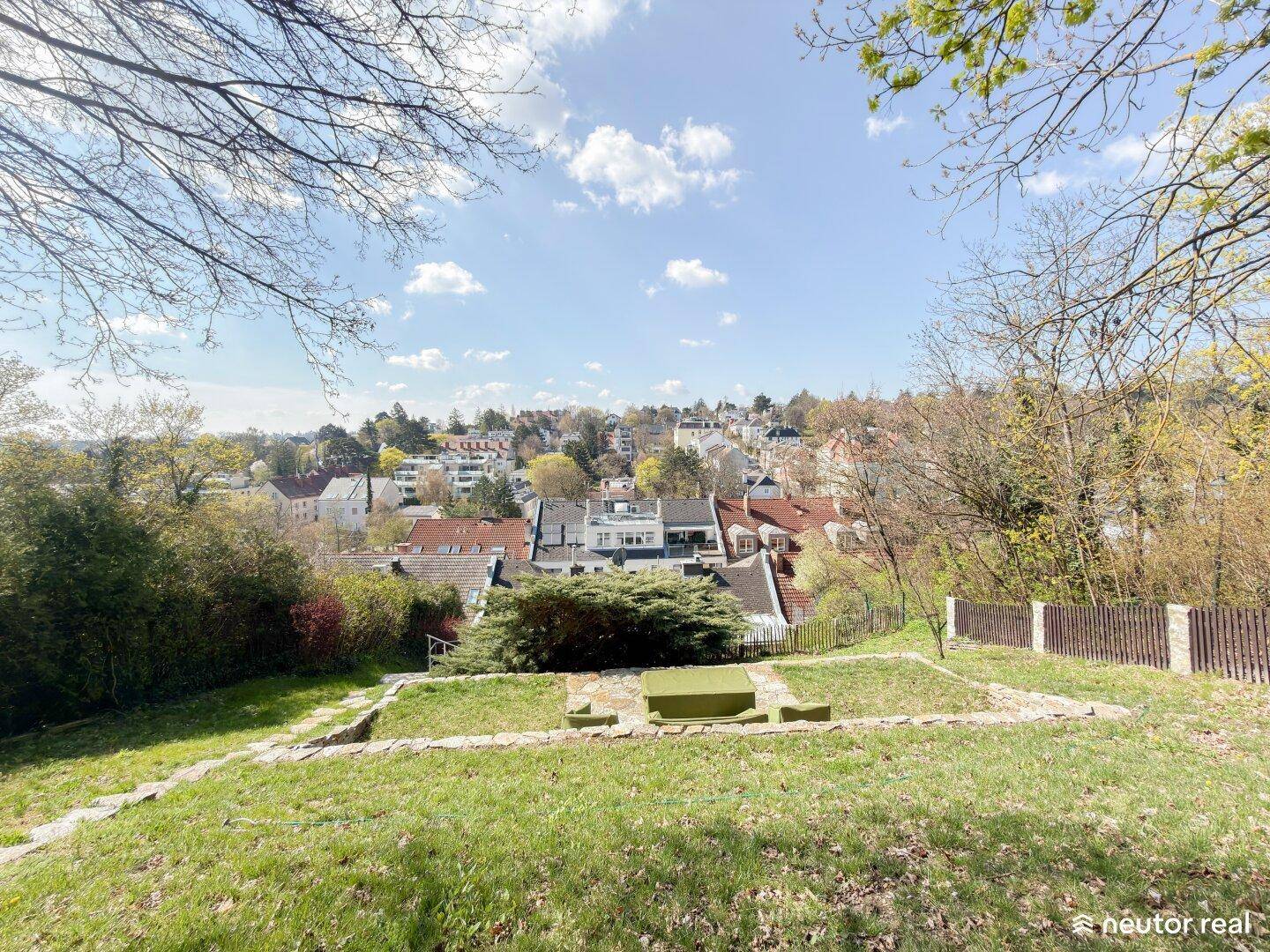 Grüner Gartenbereich auf einem Hügel mit Sitzbank und weitem Blick über die Stadt.