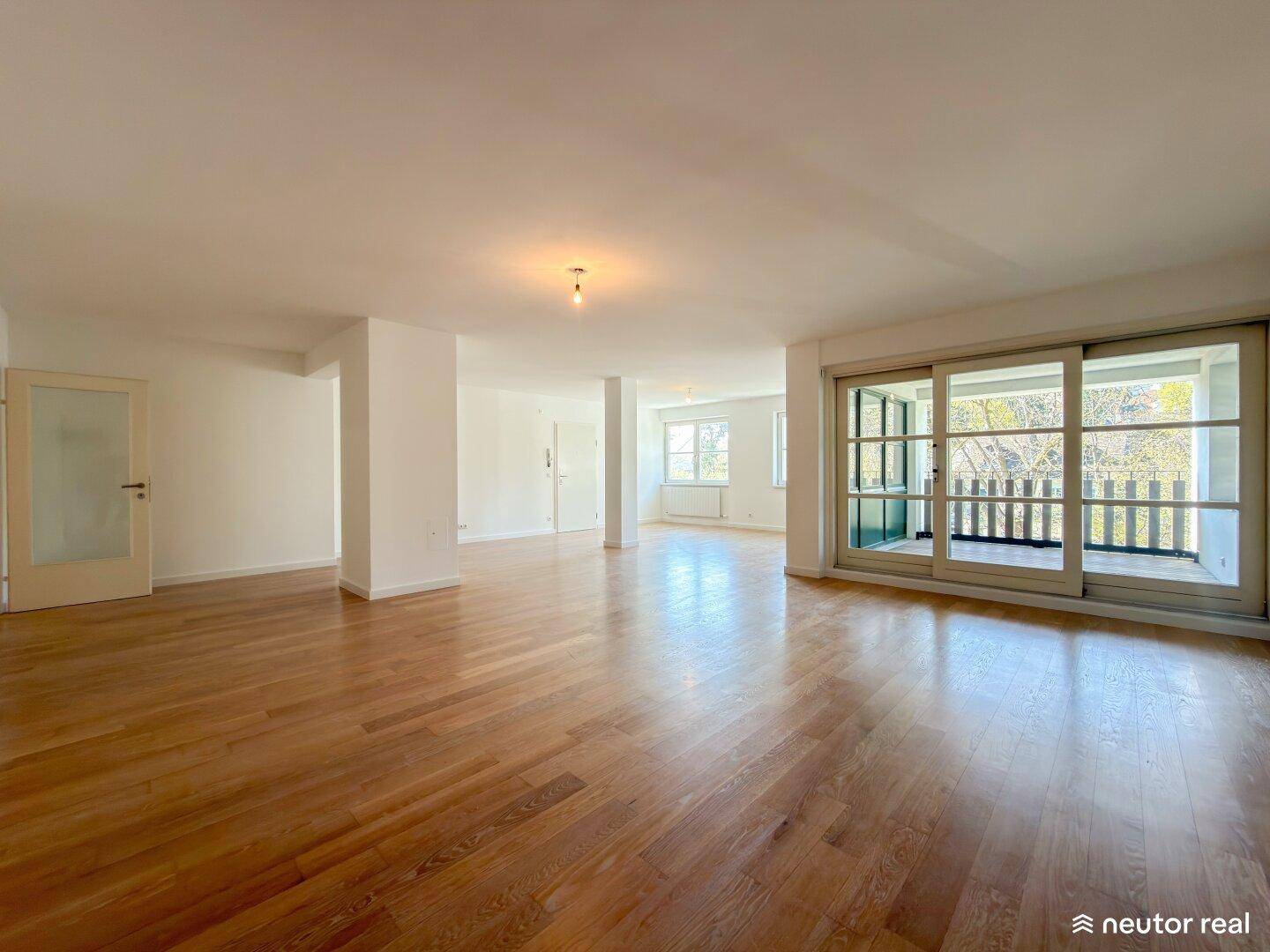 Großer, heller Wohnbereich mit Parkettboden und Zugang zum Balkon.