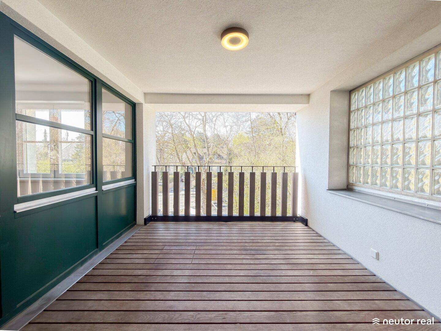 Heller Balkon mit Holzfußboden und Blick ins Grüne.