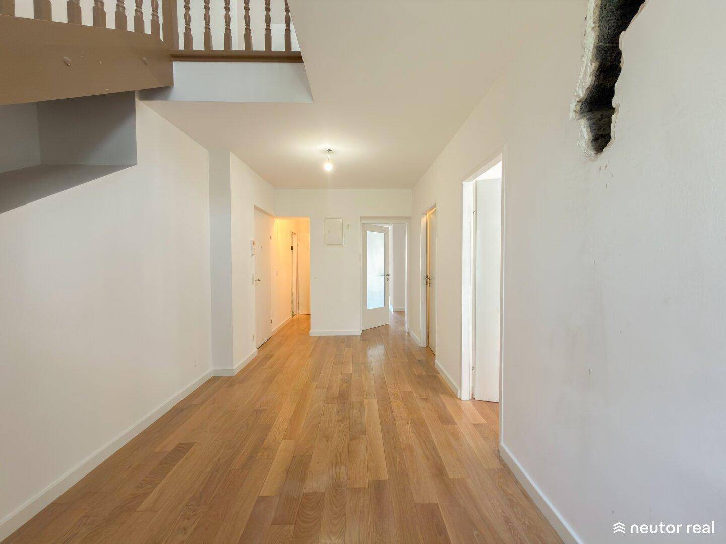 Heller Flur mit Holztreppe und Parkettboden, führt zu weiteren Räumen.