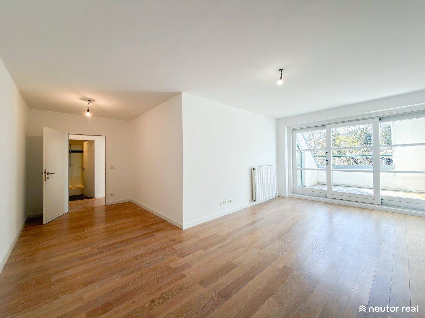 Heller Raum mit Parkettboden und Schiebetür zum Balkon.