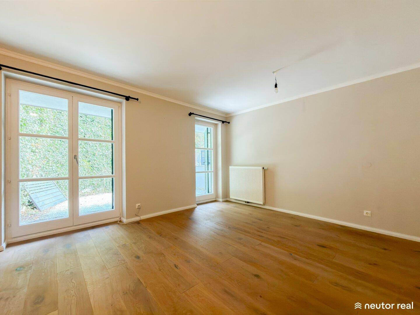Heller Raum mit Holzboden und zwei französischen Türen, die Zugang zu einem Außenbereich bieten.