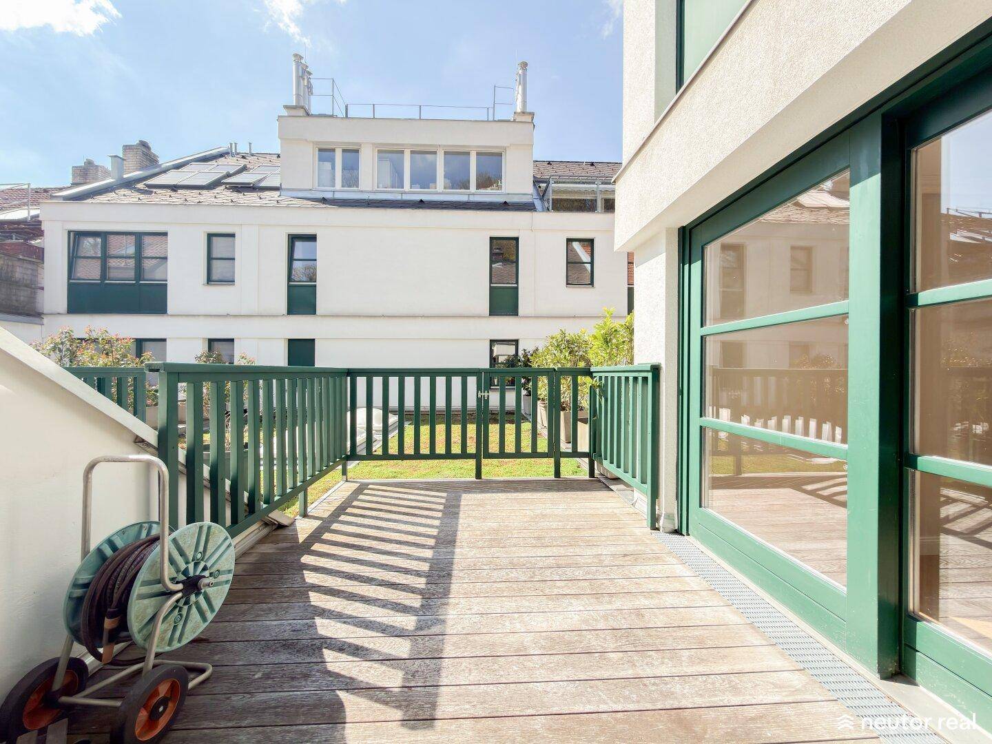 Geräumiger Balkon mit Holzbelag und grünen Geländern, bietet einen Blick auf die umliegenden Gebäude.