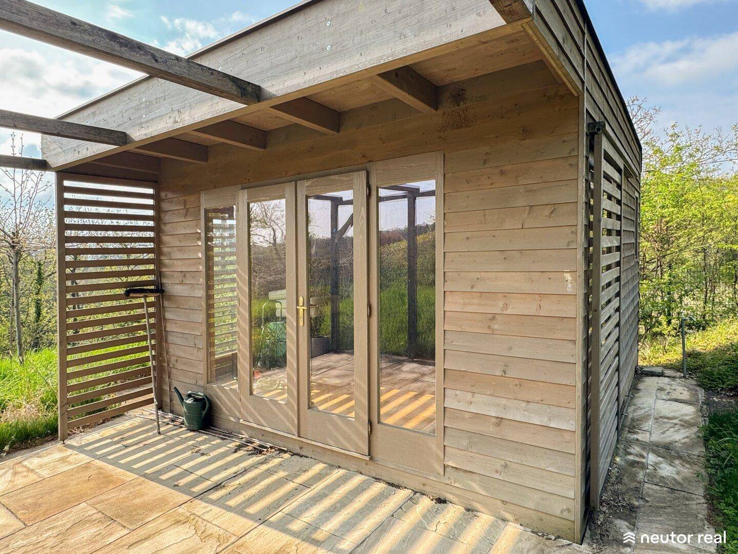 Detailansicht der Holzfassade mit Glastüren und einer kleinen gepflasterten Terrasse.