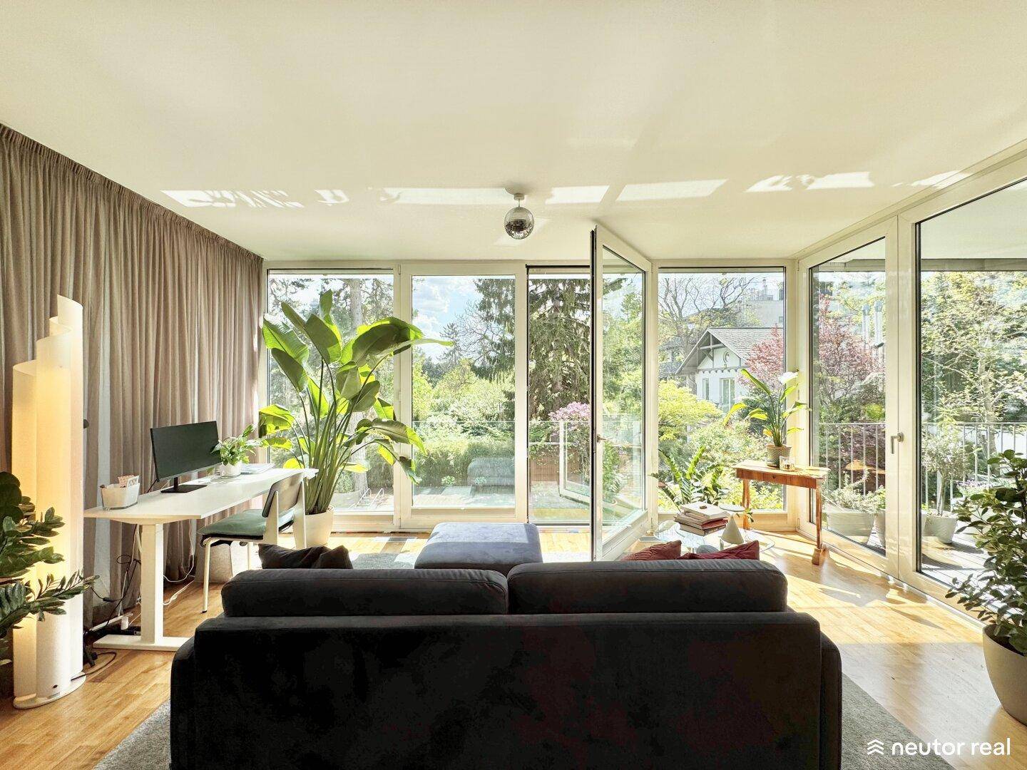 Lichtdurchflutetes Wohnzimmer mit Arbeitsbereich und großen Glasfronten zum Garten.