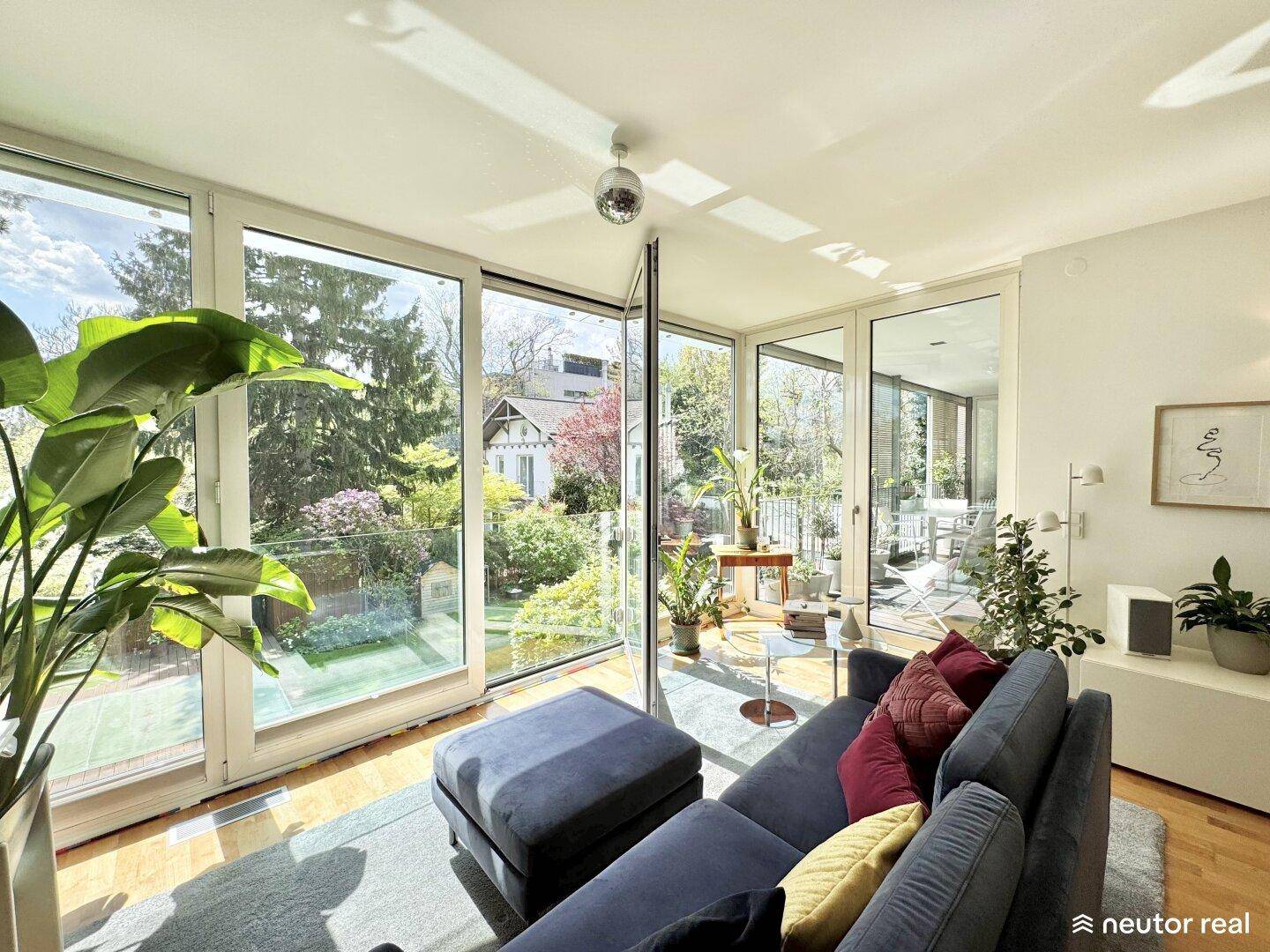 Helles Wohnzimmer mit großen Fensterfronten, die einen schönen Blick ins Grüne bieten.