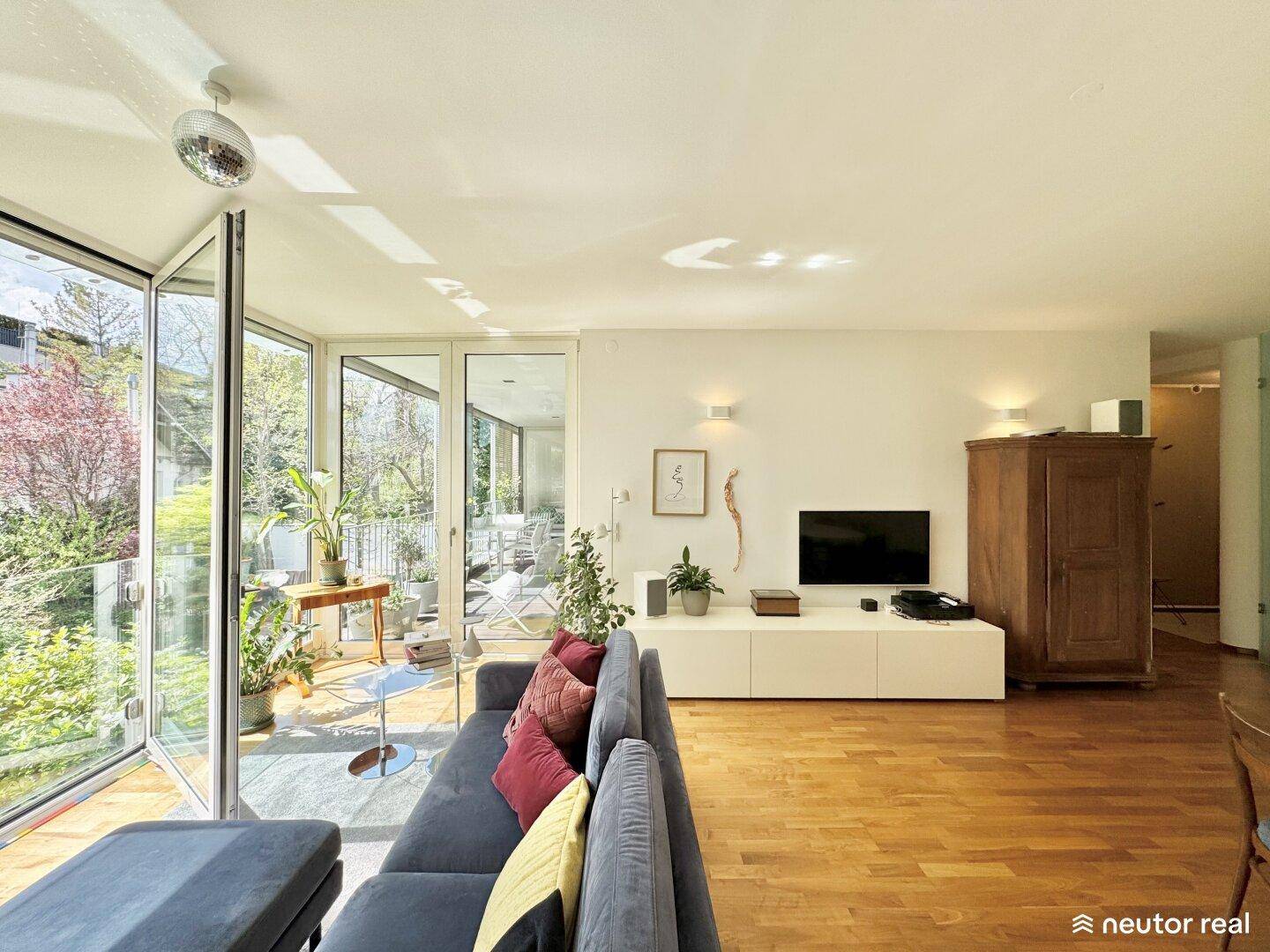 Geräumiges Wohnzimmer mit Holzboden, moderner Einrichtung und Zugang zu einem sonnigen Außenbereich.