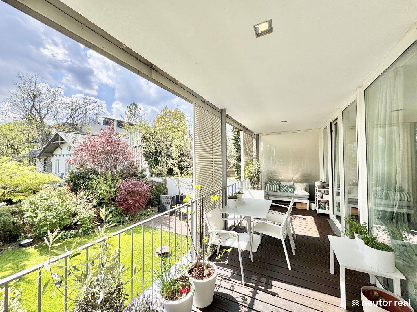 Großer, überdachter Balkon mit Esstisch und Blick auf den grünen Gartenbereich.