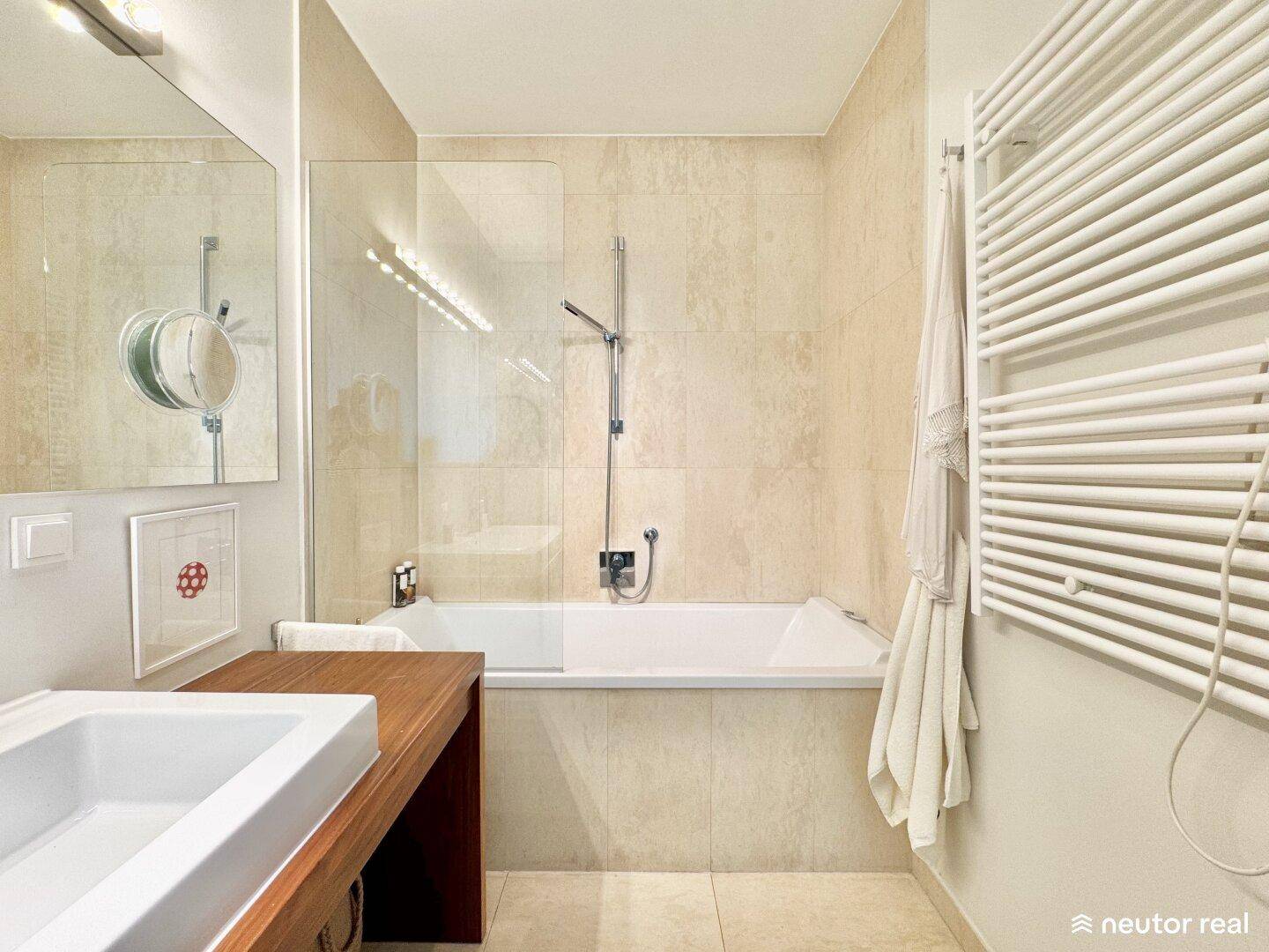 Helles Badezimmer mit Badewanne, beigefarbenen Fliesen und modernem Design.
