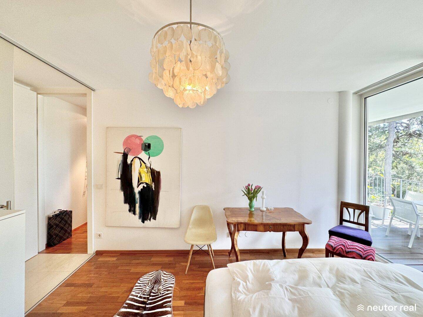 Helles Schlafzimmer mit Holzboden, Kunst an der Wand und Zugang zum Außenbereich.