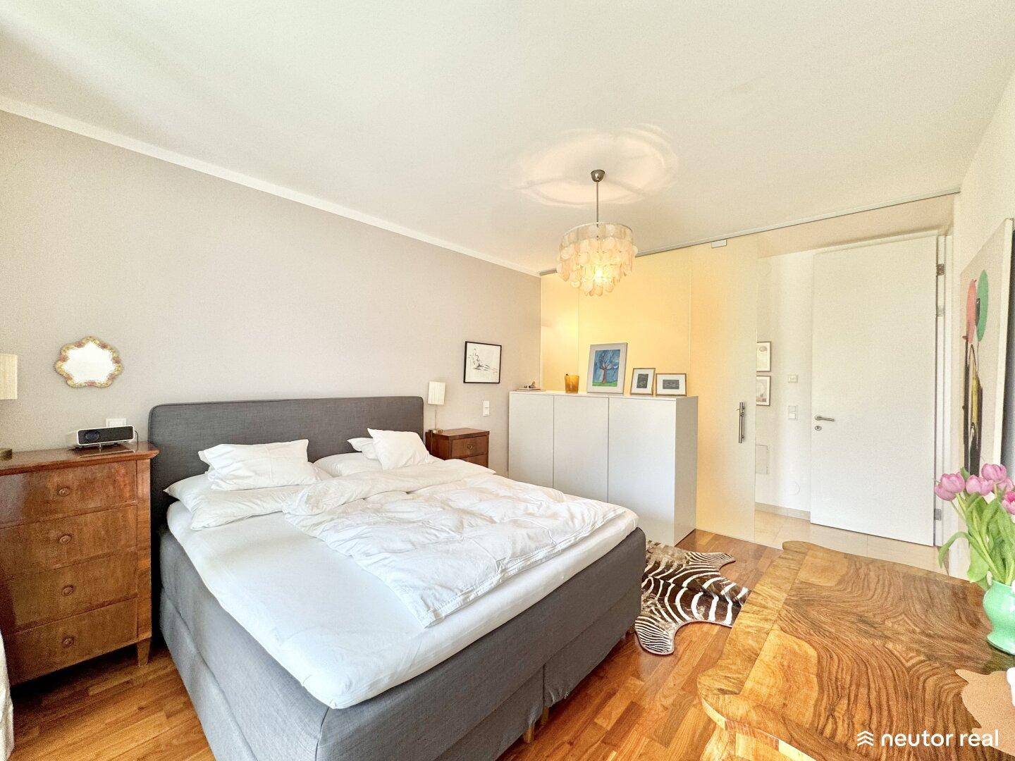 Gemütliches Schlafzimmer mit Holzboden, großem Bett und moderner Beleuchtung.