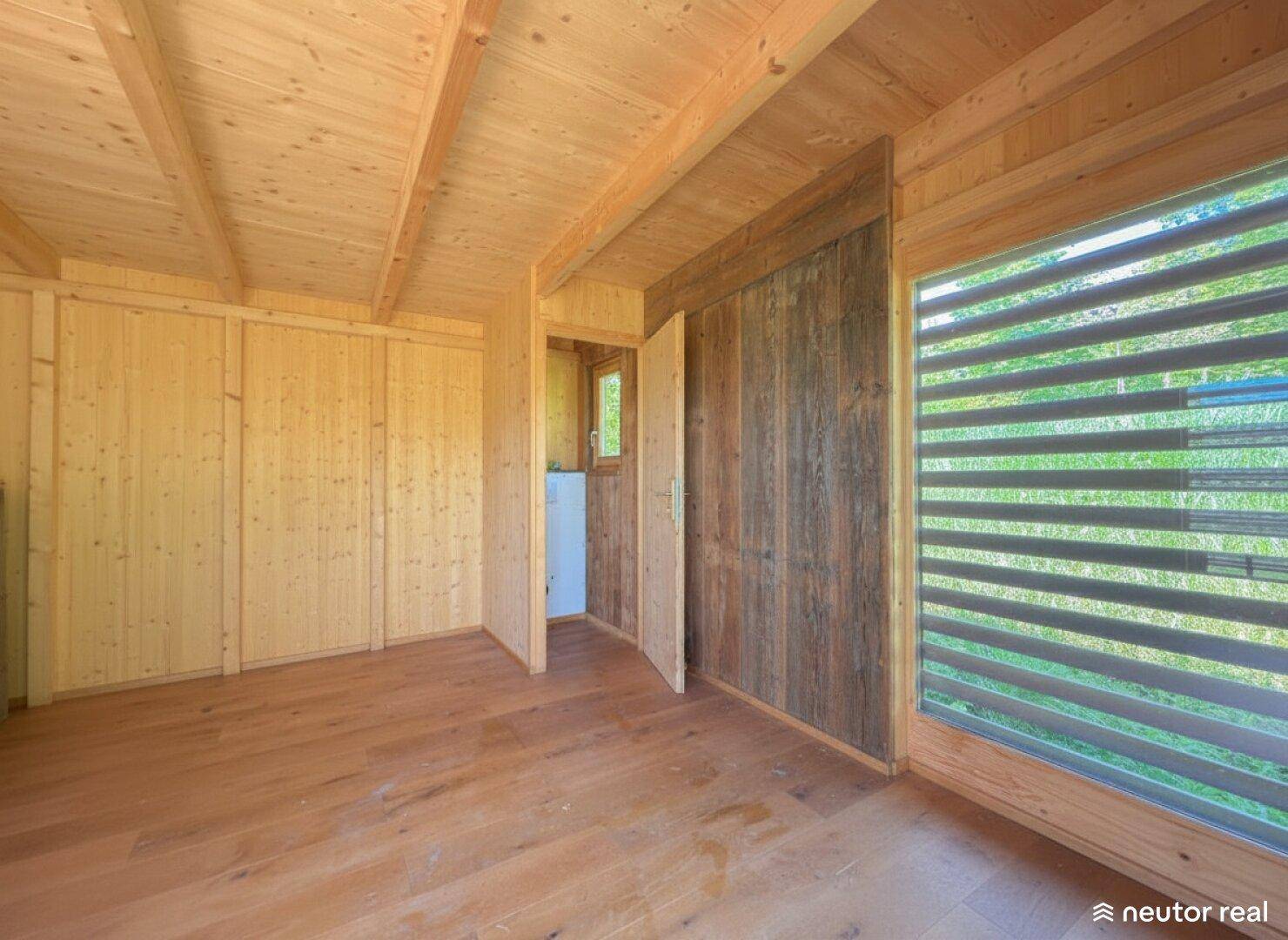 Heller Innenraum des Holzhauses mit Holzboden, Holzverkleidung und großen Fenstern.
