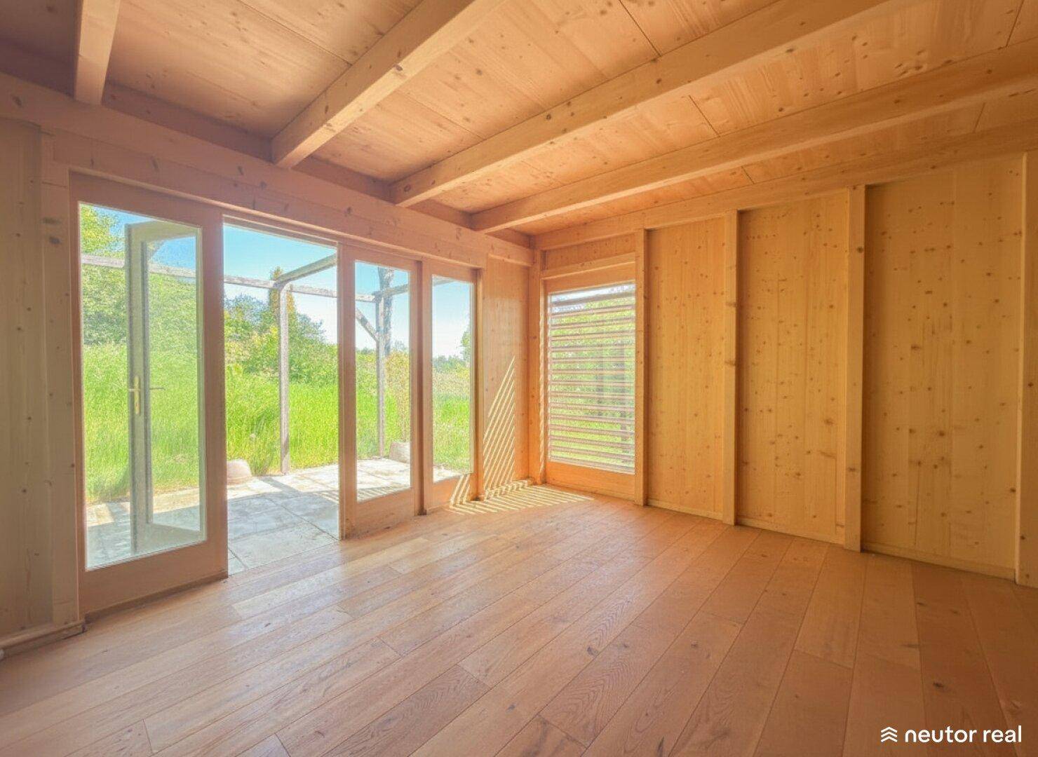 Lichtdurchfluteter Raum im Holzhaus mit Holzboden und Zugang zur Außenterrasse.
