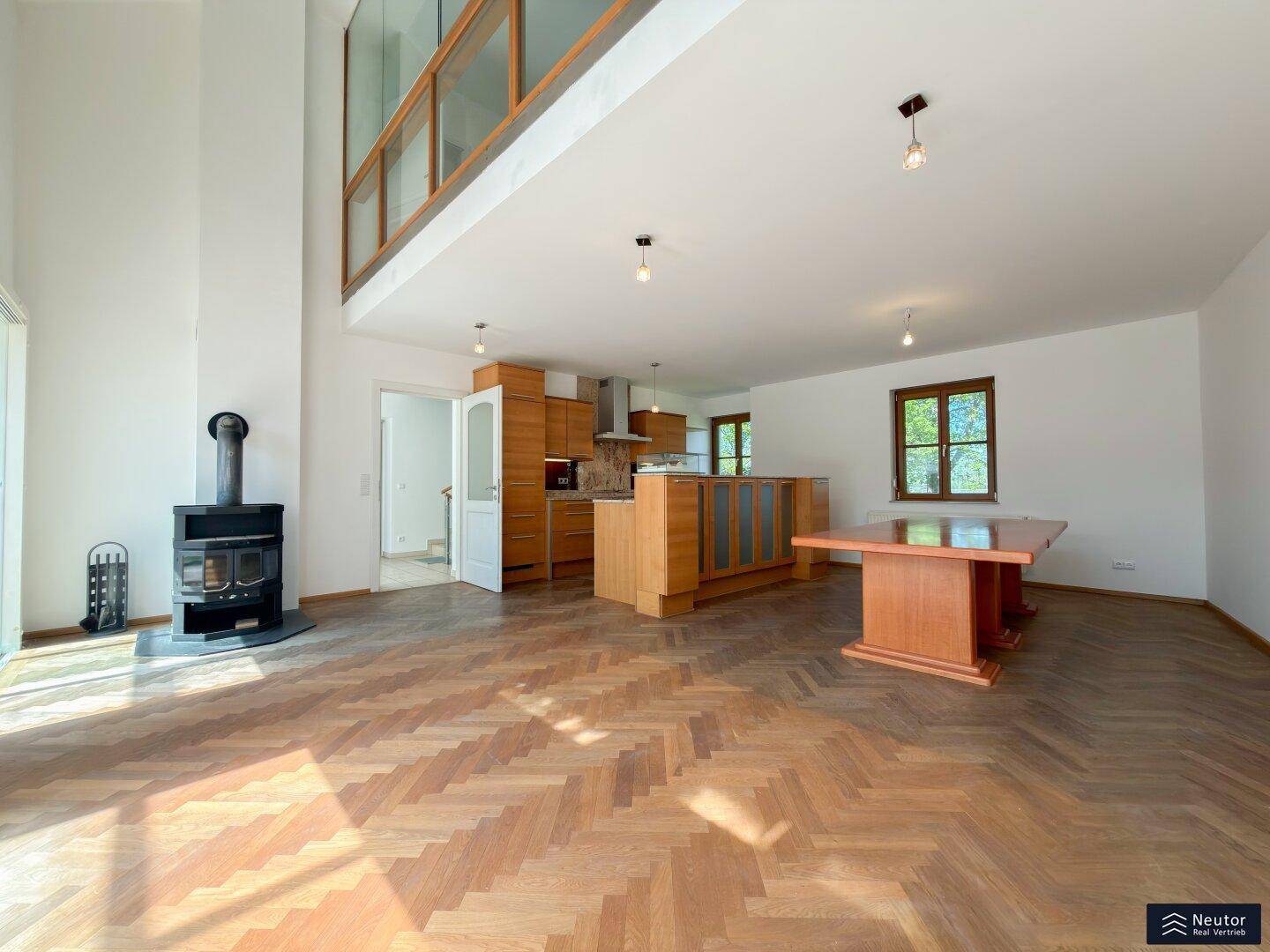 Offener Wohnbereich mit Holzboden, Kaminofen und integrierter Küche im Hintergrund.