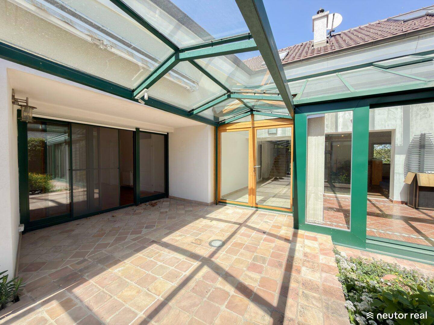 Geräumige Terrasse mit Terrakottaboden und Zugang zu einem verglasten Anbau, ideal für Outdoor-Living.